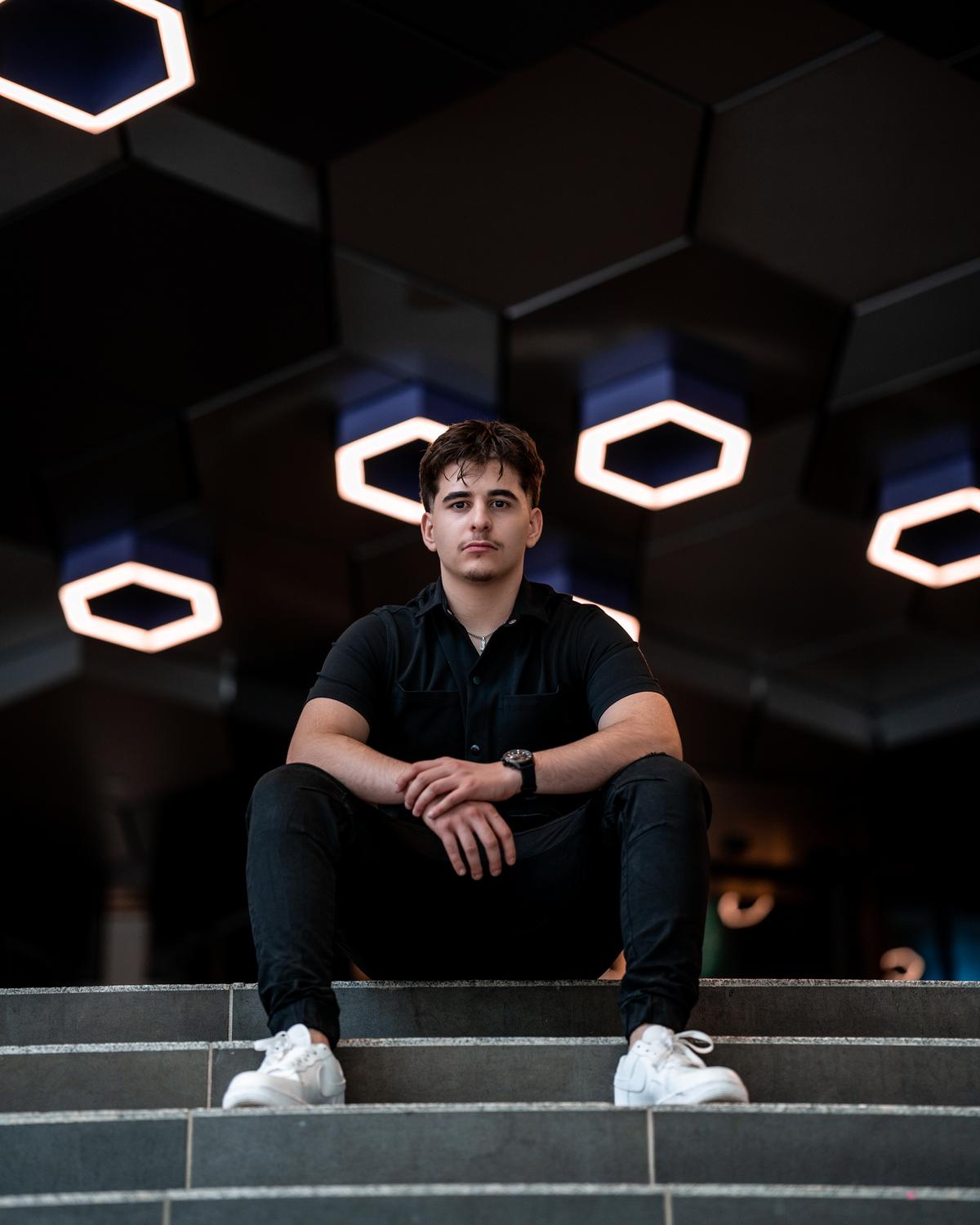 Mohsen Carter sitting on steps under hexagon lights